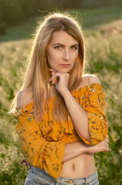 Genç sarışın beyaz kadın model yaz akşamı çayırda eğleniyor.