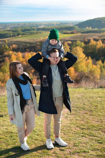 白种人的年轻父母与他们的儿子在山顶上玩耍 秋天到来了 图库图片