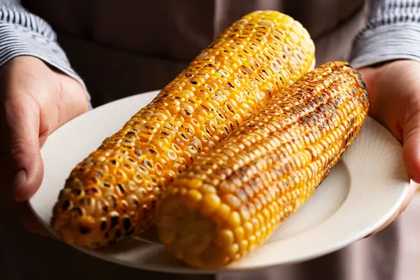 白人男性的手拿着烤着甜玉米的盘子 免版税图库图片