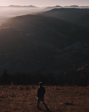 Genç bir adam sonbahar sabahları güzel dağların önünde yürür. Tek renkli panoramik görünüm.