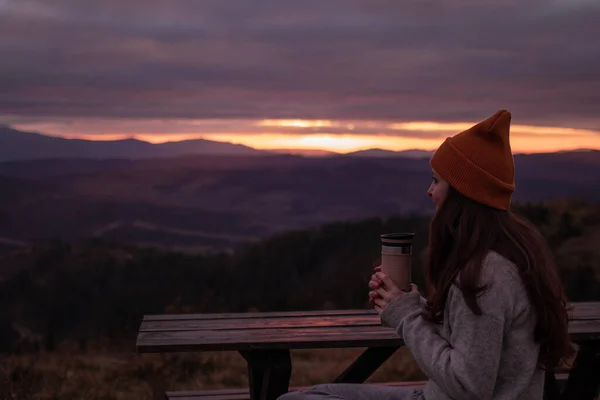 Genç Bir Kadın Ahşap Bankta Termosla Oturuyor Günbatımı Dağlarının Manzarasına — Stok fotoğraf