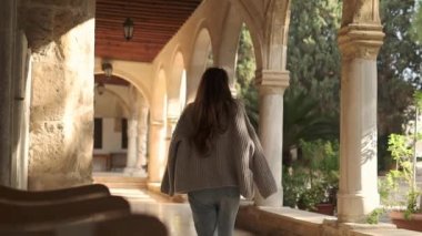 A young woman from behind is walking near the beautiful building with arches, lanterns and potted plants in Panagia Chrisopolitissa, Larnaca, Cyprus. 