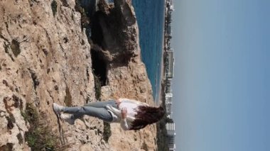 A young carefree woman is walking at the edge near sea caves love bridge in Ayia Napa, Cyprus