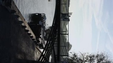 Nehir kenarında sakin bir sabahın dikey videosu. Köprüde mavi gökyüzü olan insanlar var.