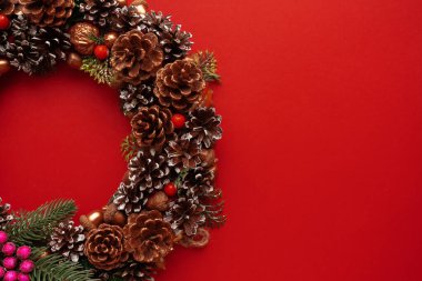 Çam kozalaklı Noel süsü, kırmızı arka planda süslü Noel çelengi. Noel havası