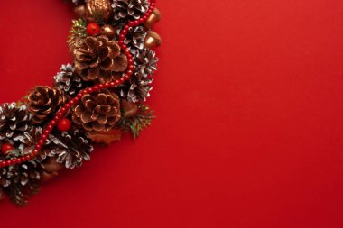 Çam kozalaklı Noel süsü, kırmızı arka planda süslü Noel çelengi. Noel havası