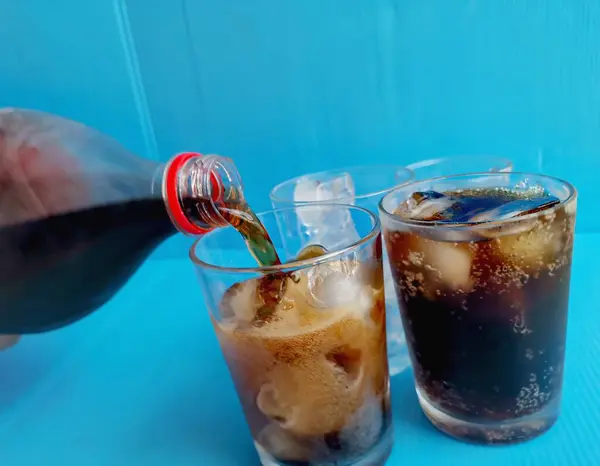 Verter Bebida Cola Sobre Vaso Con Hielo Sobre Fondo Azul Imágenes de stock libres de derechos