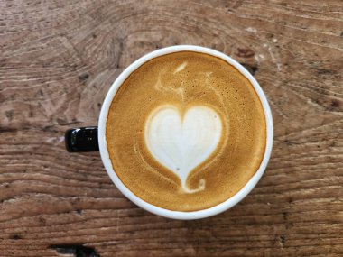 Kalp kahvesi, sütlü sanat köpüğü ahşap masa arkasında.