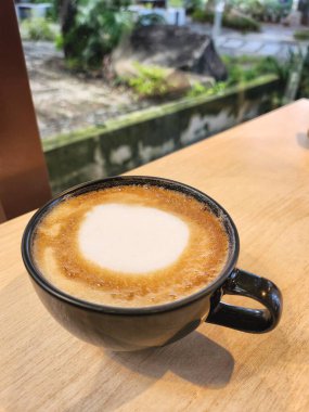 Süt köpüklü kahve, ahşap masa arkasında.