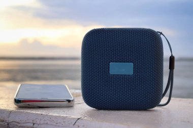 Mavi bluetooth hoparlörü ve kumsaldaki akıllı telefon.