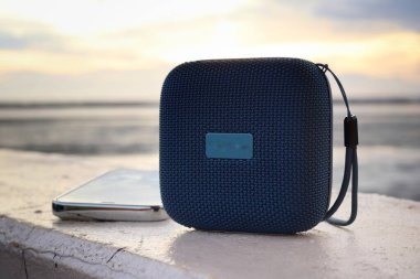 Mavi bluetooth hoparlörü ve kumsaldaki akıllı telefon.