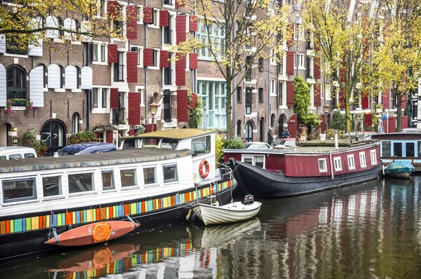 Amsterdam 'da geniş bir kanal ve rıhtımda tekneler ve arka planda evler var..