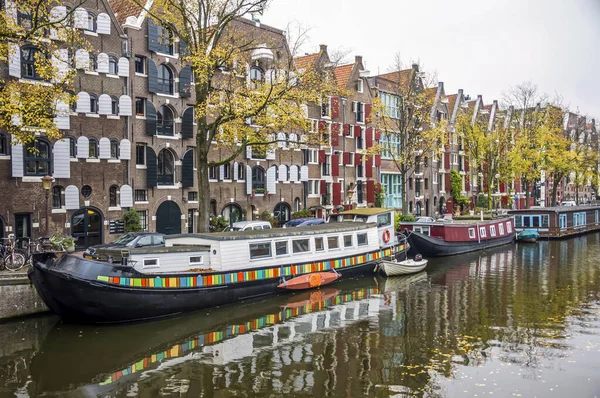 Amsterdam 'da geniş bir kanal ve rıhtımda tekneler ve arka planda evler var..