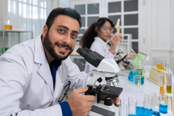 Smiling scientist with beard in white laboratory coat working with microscope for research in scientific research laboratory