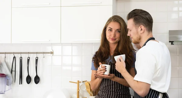 快乐甜蜜的年轻夫妇一起在厨房喝咖啡 拿着杯子 聊着天 在家里喝着热饮 享受着早晨的闲暇时光 — 图库照片
