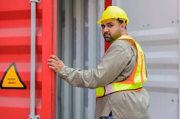 Male container logistic worker in yellow helmet and safety vest opening container door for inspection condition of empty container before loading finish goods at cargo shipping yard