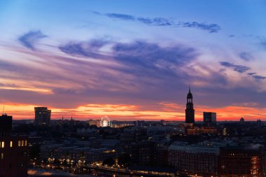 Dansçı kuleleri olan Hamburg şehrinin hava manzarası Dom 'un Dönme dolabı ve gün batımında St. Michaelis kilisesi.