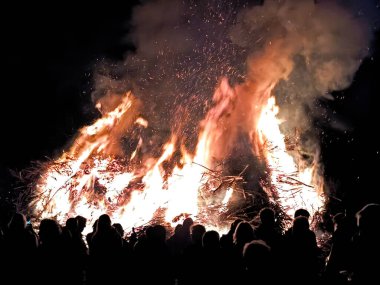 A huge easter fire blazes at night, captivating a crowd with the flames, under a dark sky