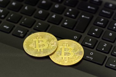 Dijital para biriminin ve finansal yeniliğin yükselişini simgeleyen iki altın Bitcoin dizüstü bilgisayarın klavyesinde dinleniyor.