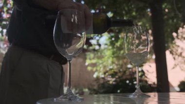 Bir adam bahçede iki bardak beyaz şarap servis eder. Yavaş çekim