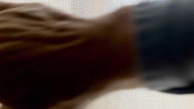 Bir adamın eli perdeyi çeker ve bulanık bir arka plan görülür