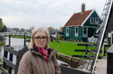 Olgun kadın, bölgenin kırsal yaşam tarzı, turizmi ve mimari karakteristik özelliklerini temsil eden geleneksel evleri, akan kanal ve yeşil çimlerin önünde, Avrupa 'nın manzaralı bir köyünde poz veriyor..