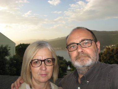 Gün batımında sakin bir günde arka planda yeşillik ve dağlar olan bir rıhtımın yanında poz veren gözlüklü iki yetişkinin yakın plan fotoğrafı..