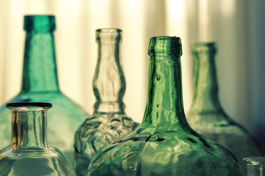 Şişeler ve cam sürahiler arka planda.