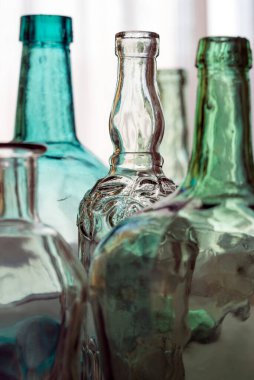 Şişeler ve cam sürahiler arka planda.