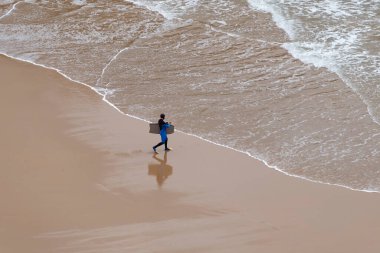 SANTANDER, İspanya - 11 Mart 2015: Yerel çocuk bir kış sabahı sahilde sörf tahtasıyla yürüyor 