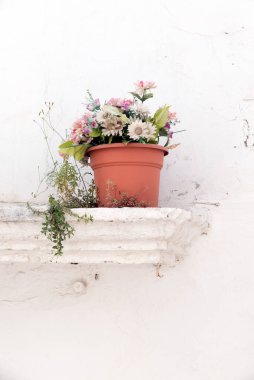 Yapay çiçeklerle bembeyaz bir duvarın kenarında saksı