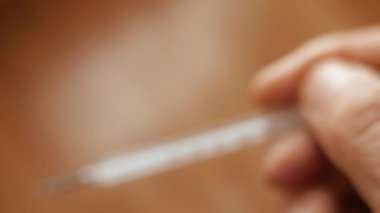 Bir adam elinde cıva klinik termometresi tutuyor.