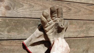 Bir adam ahşap bir masadan iş eldivenlerini alır ve onları takar.