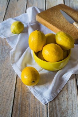Tahta arka planda sarı bir kasede taze limonlar.