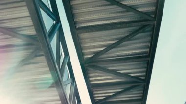 Aşağıdan görünen bir endüstriyel geçitin metal yapısında dolaşıyordu.