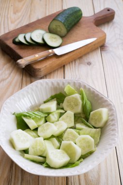 Tahta bir masada beyaz bir kasede salatalık salatası.