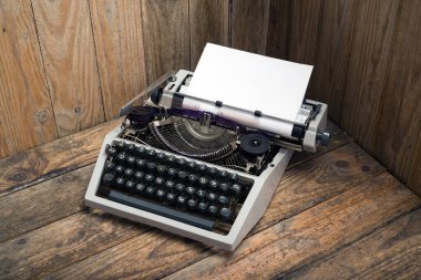 Tahta masa üzerinde beyaz kağıt sayfası olan antika bir daktilo. Eski tarz natürmort