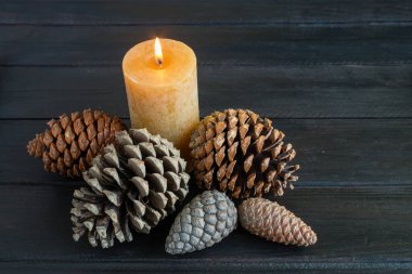 Çam kozalaklı Noel süslemeleri ve siyah odunda yanan mumlar.