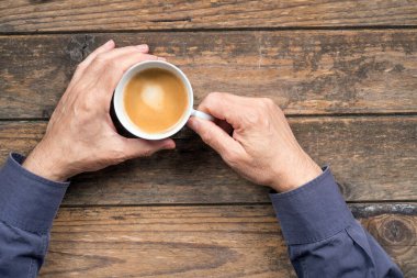 Erkek elleri ve bir fincan kahve, tahta arka planda.