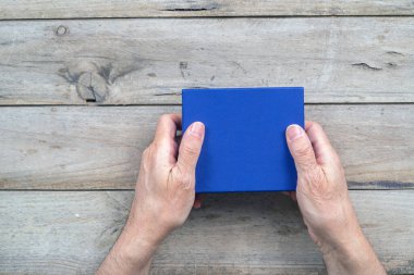 Mavi hediye kutusunu ahşap arka planda tutan adam.