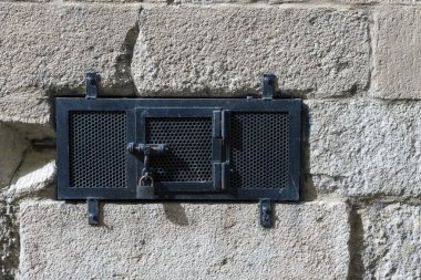 Taş duvarda asma kilit olan kapalı metal bir kapı.