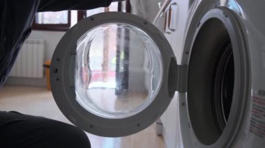 Çamaşır makinesine çamaşır koyan, ev işlerini, temizliği ve günlük hayatı ön plana çıkaran bir adamın yakın çekimi. Dekor modern görünüyor, tipik bir ev çamaşırını tasvir ediyor..