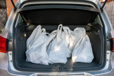 Alışverişi, rahatlığı ve ulaşımı temsil eden market ve eşyalarla dolu çok sayıda beyaz plastik alışveriş torbalarını gösteren açık bir araba bagajı. Ayak işleri, modern yaşam tarzları ve ev işleri için ideal..