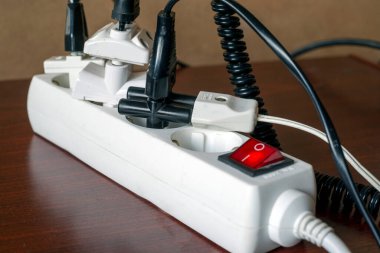 Ev ya da ofis ortamlarında uygun uygulama kullanımına yönelik tedbirleri vurgulayan birden fazla fiş ve kabloya bağlı aşırı yüklü bir elektrik güç şeridinin yakın çekimi.