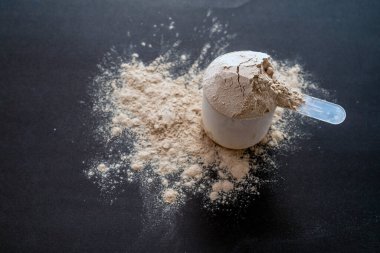 Koyu yüzeyde kepçeli protein tozu, fitness, beslenme ve sağlık odaklı yaşam tarzlarını sembolize eder..