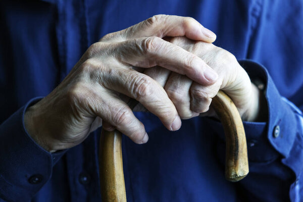 Close-up of elderly hands clasping a wooden cane, conveying themes of age, care, and suppor