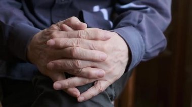 Dizlerinin üzerinde dinlenen katlanmış ellerin yakın çekim görüntüsü, sakin bir ortamda sükunet ve düşünceliliği resmediyor. Görüntü bir huzur ve içgözlem hissi veriyor.