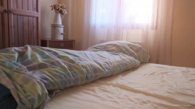 Parlak yatak odası, doğal ışık, ahşap mobilyalar, rahat bir atmosfer, ve rahat ve davetkar bir his için desenli bir yatak örtüsü. Doli.