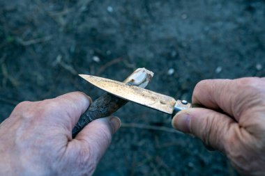 Küçük bir bıçakla sopayı ustalıkla oyan eller. Sahnede işçilik, hassasiyet ve manüel beceriler vurgulanıyor. Açık havada ahşap şekillendirmenin el işi gösteriliyor..