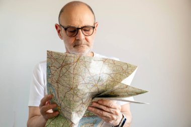 Yaşlı bir adam evin içinde dikilirken bir yol haritasını dikkatle inceliyor, keşif ve navigasyonu vurguluyor..